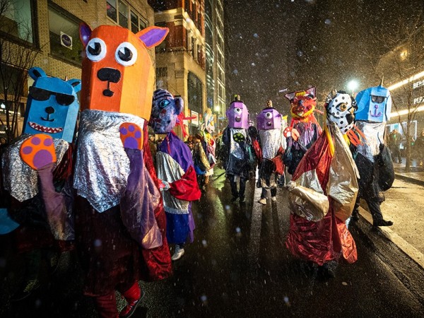 Oversized puppet costumes of various cartoon animals parade down a city street in the snow