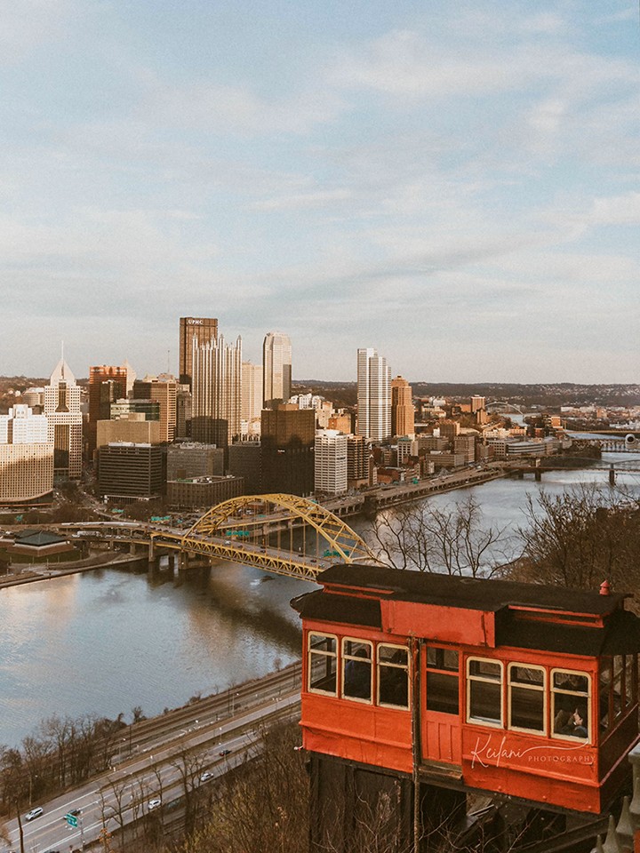 A photo of Pittsburgh's skyline, a yellow bridge, and a river, with a red trolley visible in the foreground