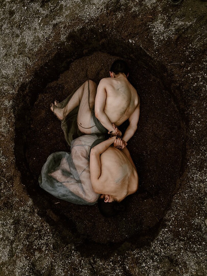 Overhead view of two nearly naked bodies, shown from behind, laying back-to-back in a ditch