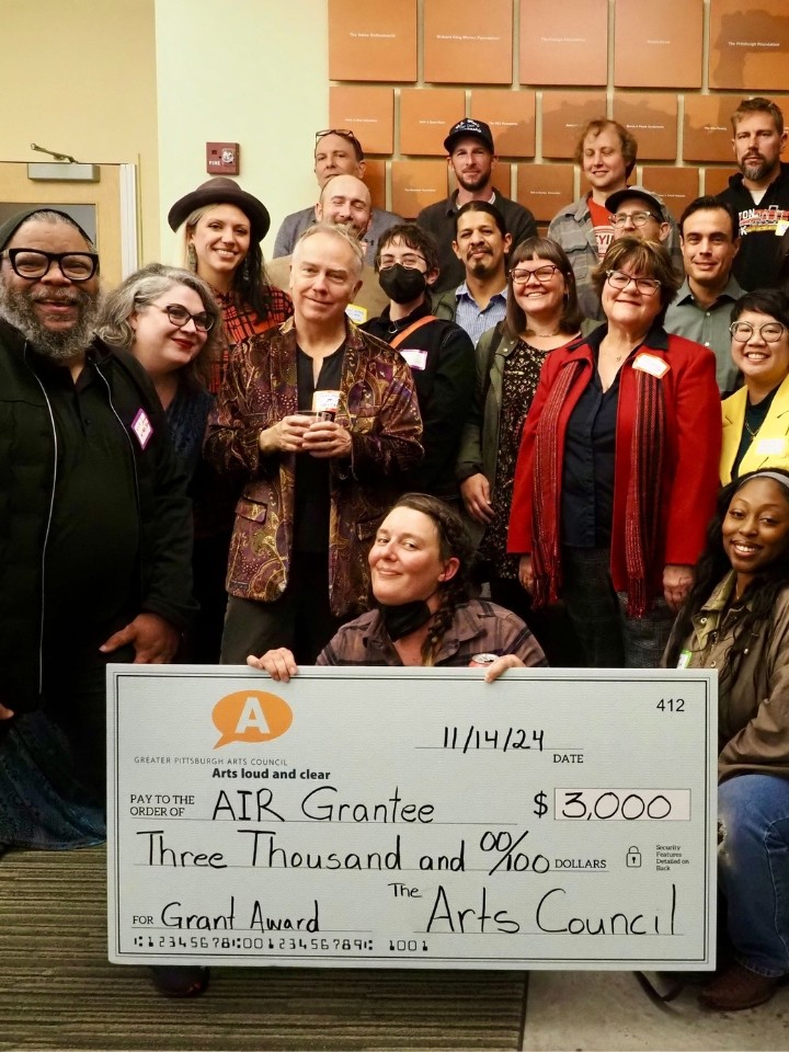 A group of over 20 people pose while holding a giant check that says Greater Pittsburgh Arts Council Air Grantee, $3,000