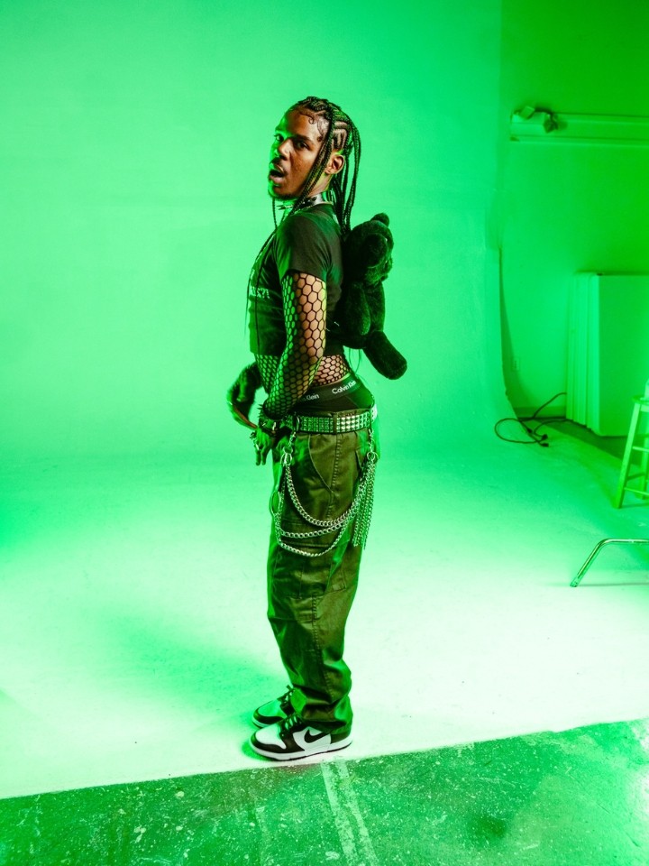 A black man standing with his side facing the camera in a room with green lighting