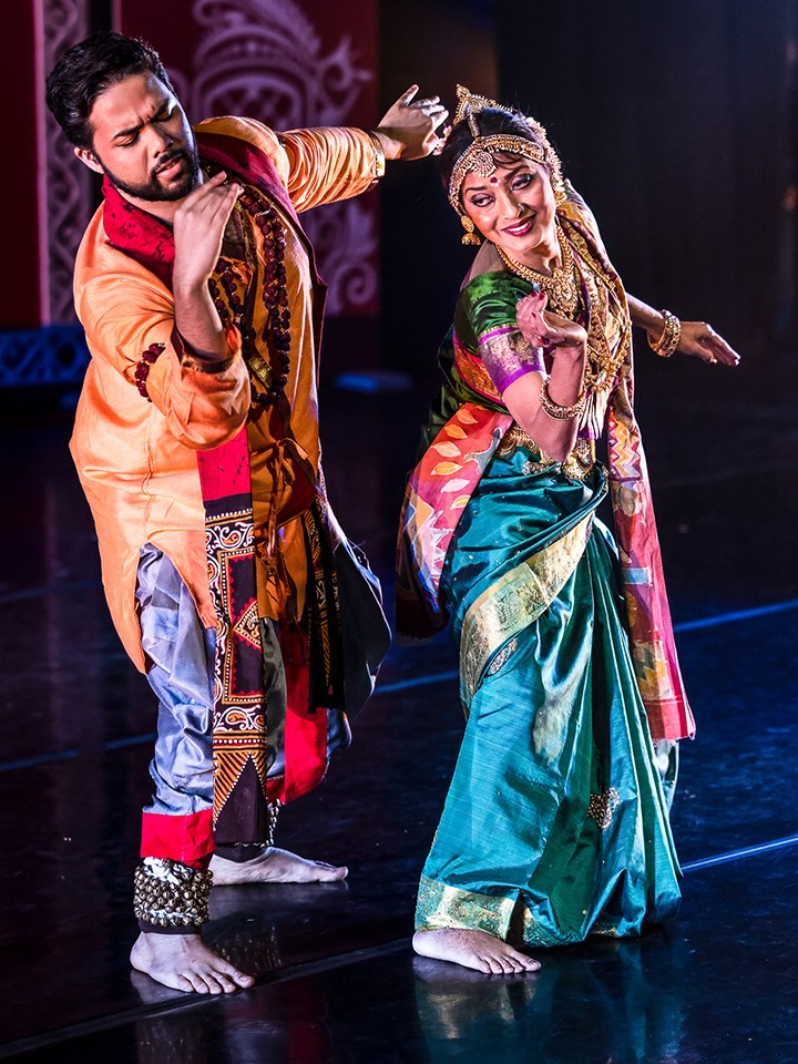 Two Indian dancers, one man and one woman, strike a dance pose while wearing traditional outfits