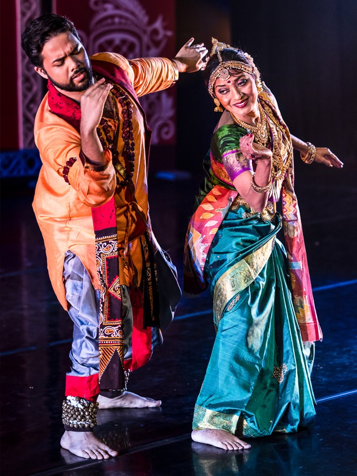 A man and a woman dressed in traditional Indian attire dance on stage