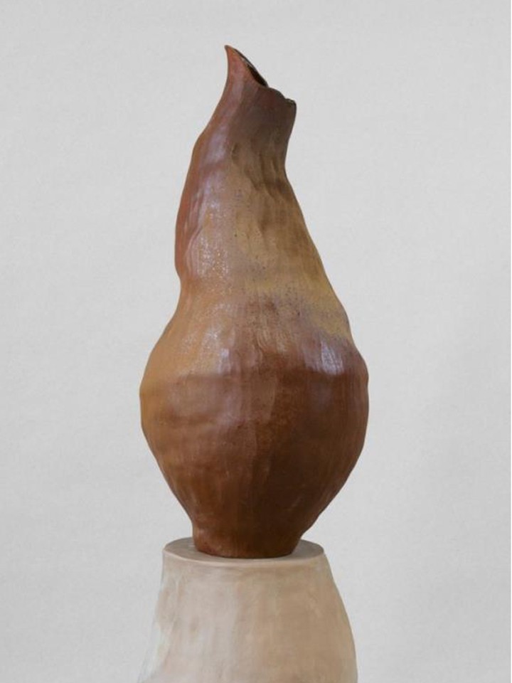 Dark reddish brown abstract ceramic sculpture sitting on a tan pedestal