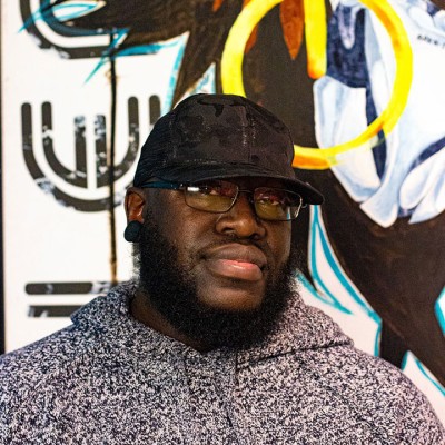 Natiq Jalil smiling directly at the camera, wearing a gray hoody and black baseball hat.