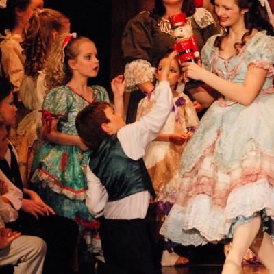 A woman dressed up in a frilly dress holds up a nutcracker to a group of children