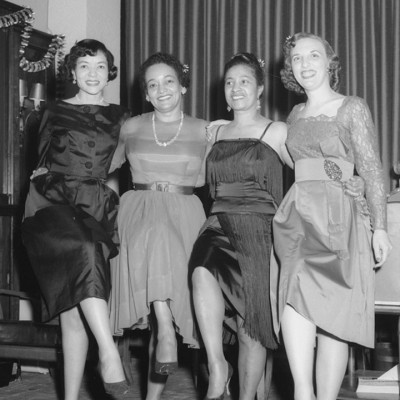 Vintage black-and-white photo of four smiling Black women in dresses posing in a row