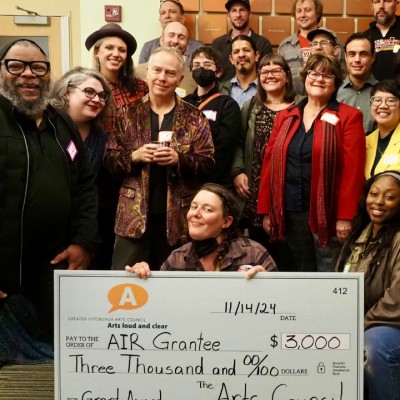 A group of over 20 people pose while holding a giant check that says Greater Pittsburgh Arts Council Air Grantee, $3,000