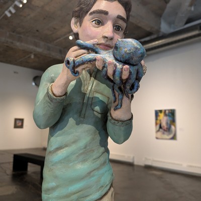 Close-up of a sculpture of a young white boy with brown hair holding an octopus in his hands, with his fingers interlocked in its tentacles