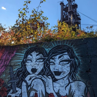 Graffiti of two girls with black lipstick and a skull with a knife in it on the side of a bridge