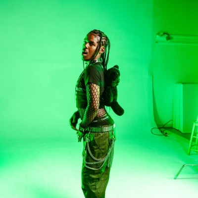 A black man standing with his side facing the camera in a room with green lighting