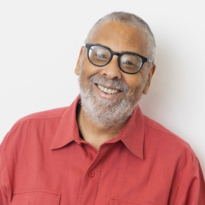 A black man with glasses wearing a red collared shirt in front of a white background