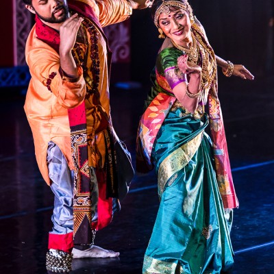 Two Indian dancers, one man and one woman, strike a dance pose while wearing traditional outfits