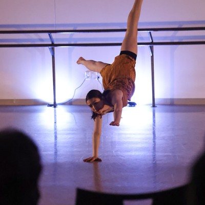 A crowd is shown watching a dancer perform while balancing themself on one arm