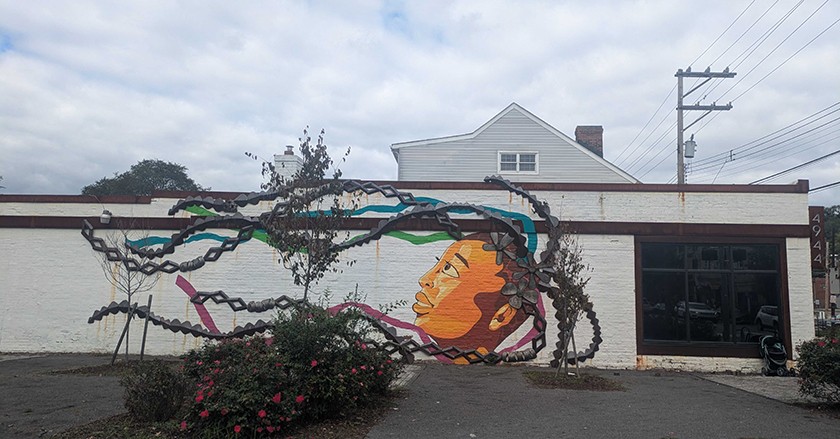 a mural on the exterior of a building showing a painted woman's face with 3-D chain objects installed to represent long hair braids