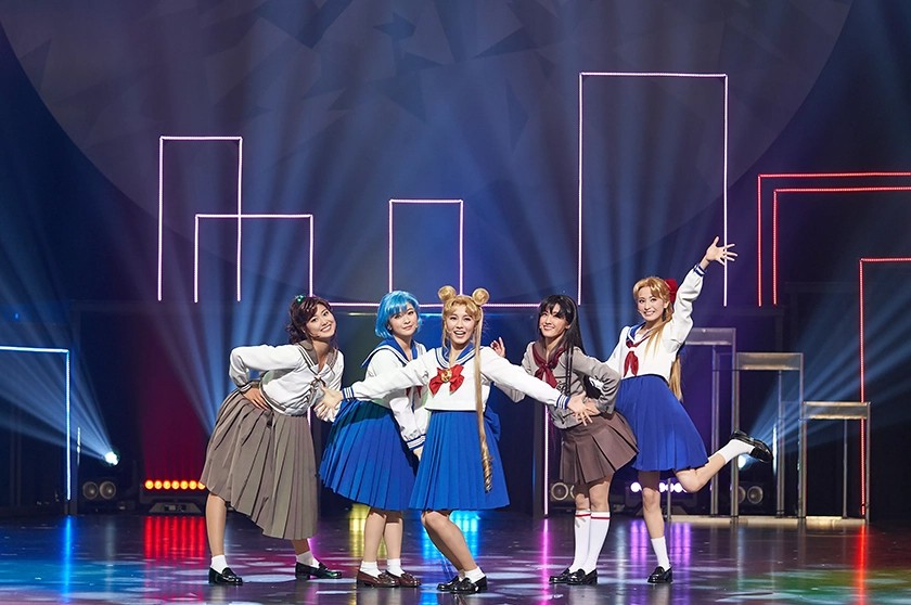 Five young women on stage dressed up in anime Sailor Moon outfits