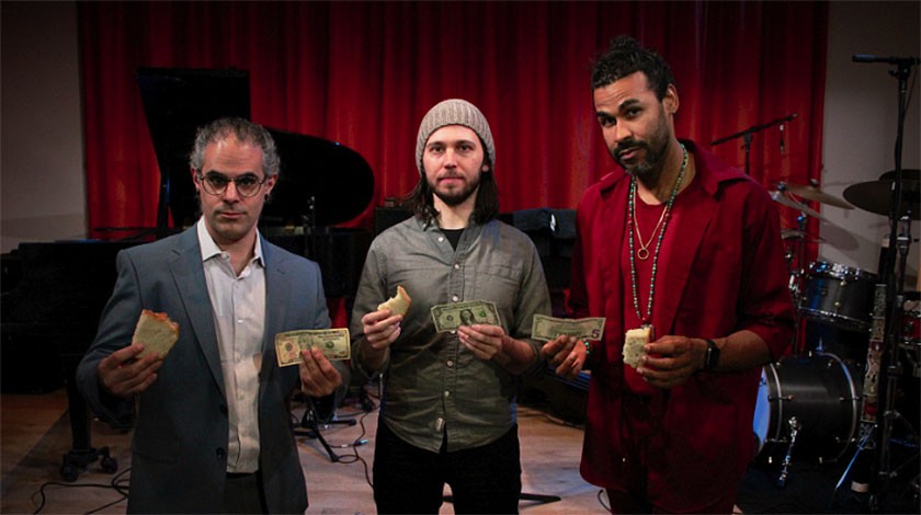 Three men stand on a stage side-by-side holding up dollar bills