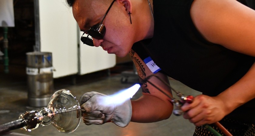 A person with protective glasses on holding a flame and glass blowing